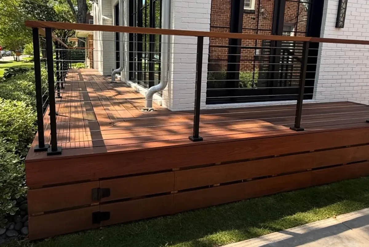 Raised hardwood front deck with horizontal skirt boards, steel posts and stainless cable rail along a white-painted brick home in West University.