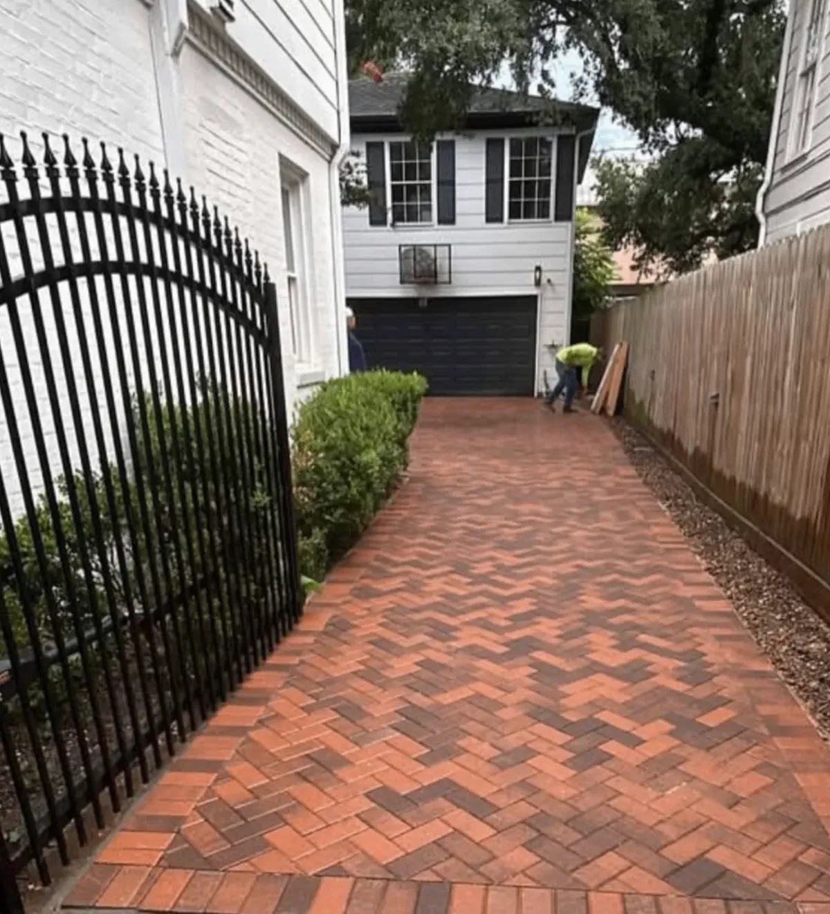 Clay-brick herringbone side drive with a soldier-course border and gravel strip between fences in West University, Houston.