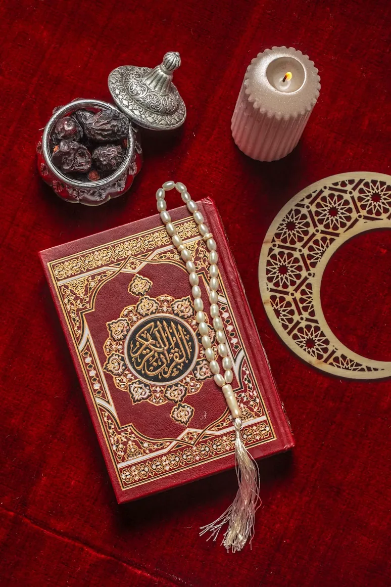 A red Qur’an with prayer beads, dates, a candle and crescent-shaped decoration.
